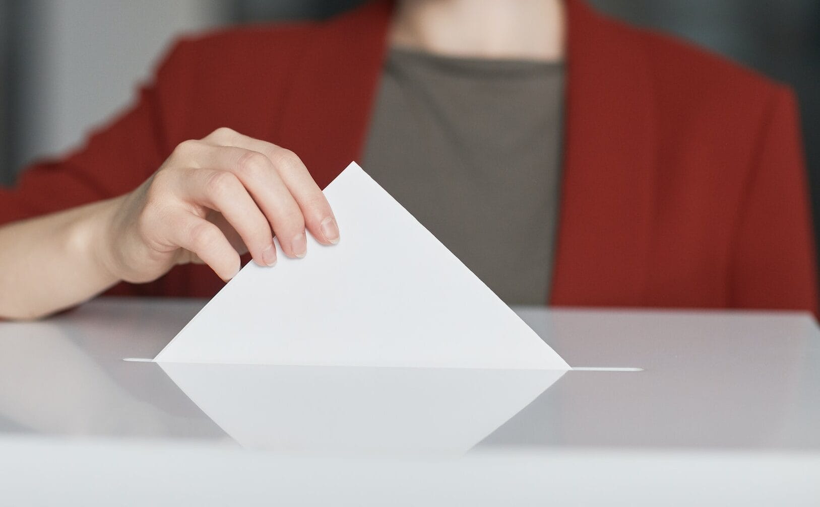 Frau in rotem Jackett wirft Zettel in Wahlurne